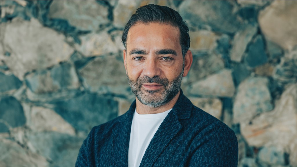 Yiannis Misirlis, Chairman at Imperio Group and LBDA, dressed in a dark blue jacket, standing in front of a stone wall