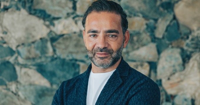 Yiannis Misirlis, Chairman at Imperio Group and LBDA, dressed in a dark blue jacket, standing in front of a stone wall